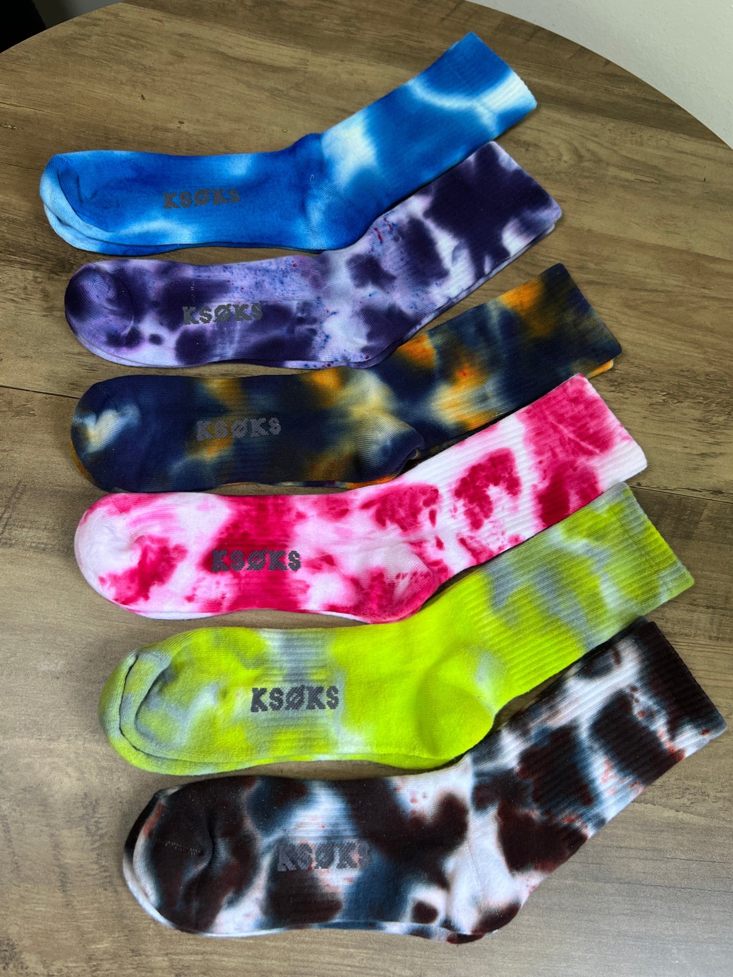 six pairs of tie-dye socks on a wooden surface