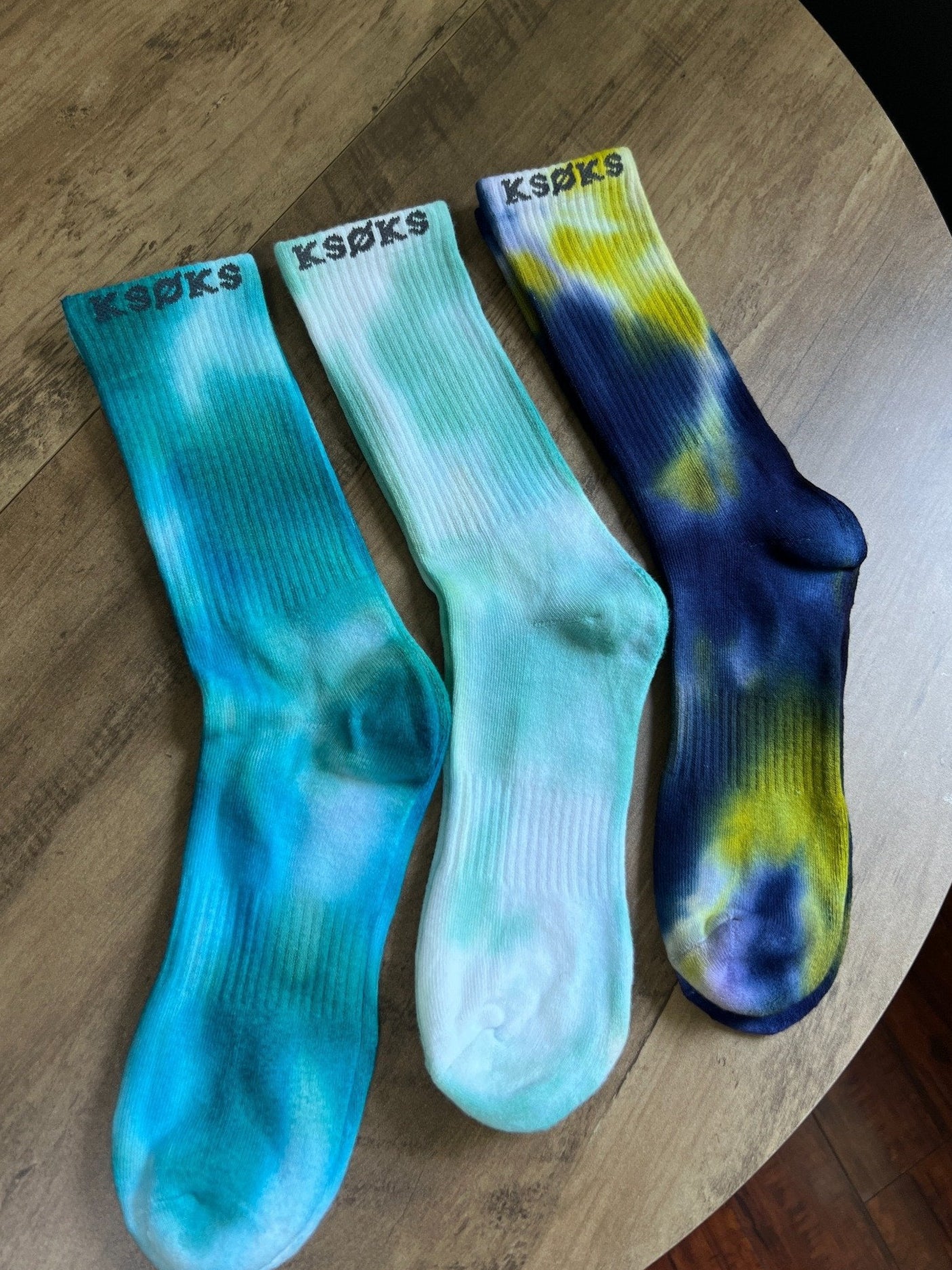 Three pairs of socks with tie-dye patterns on a wooden surface