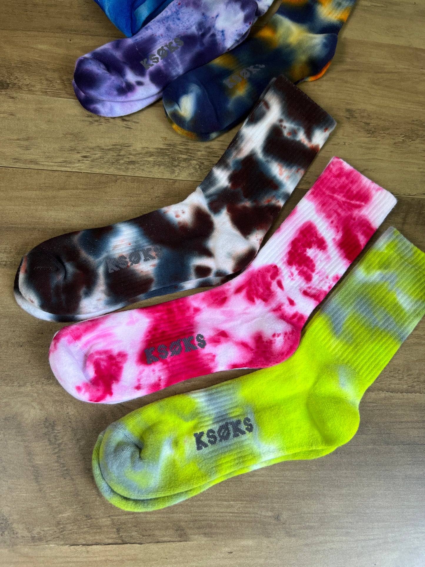 Colorful tie-dye socks with 'Ksubi' branding on a wooden surface