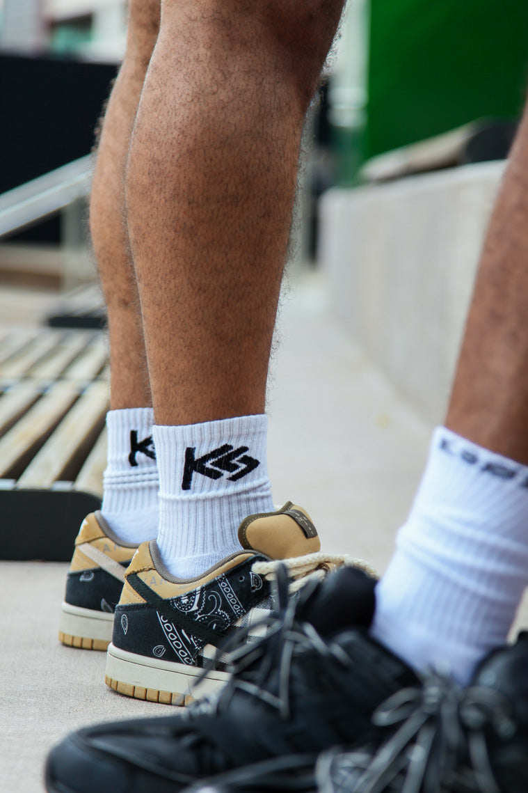 Close-up of feet wearing white socks with black logo and black sneakers on a blurred background