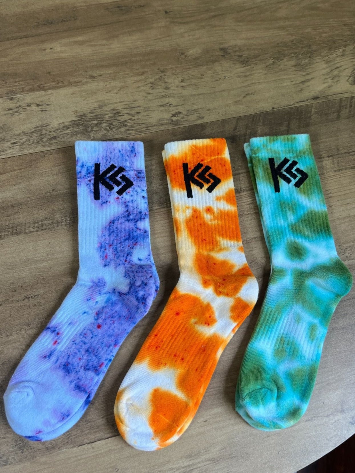 Three tie-dye socks with a logo on a wooden surface